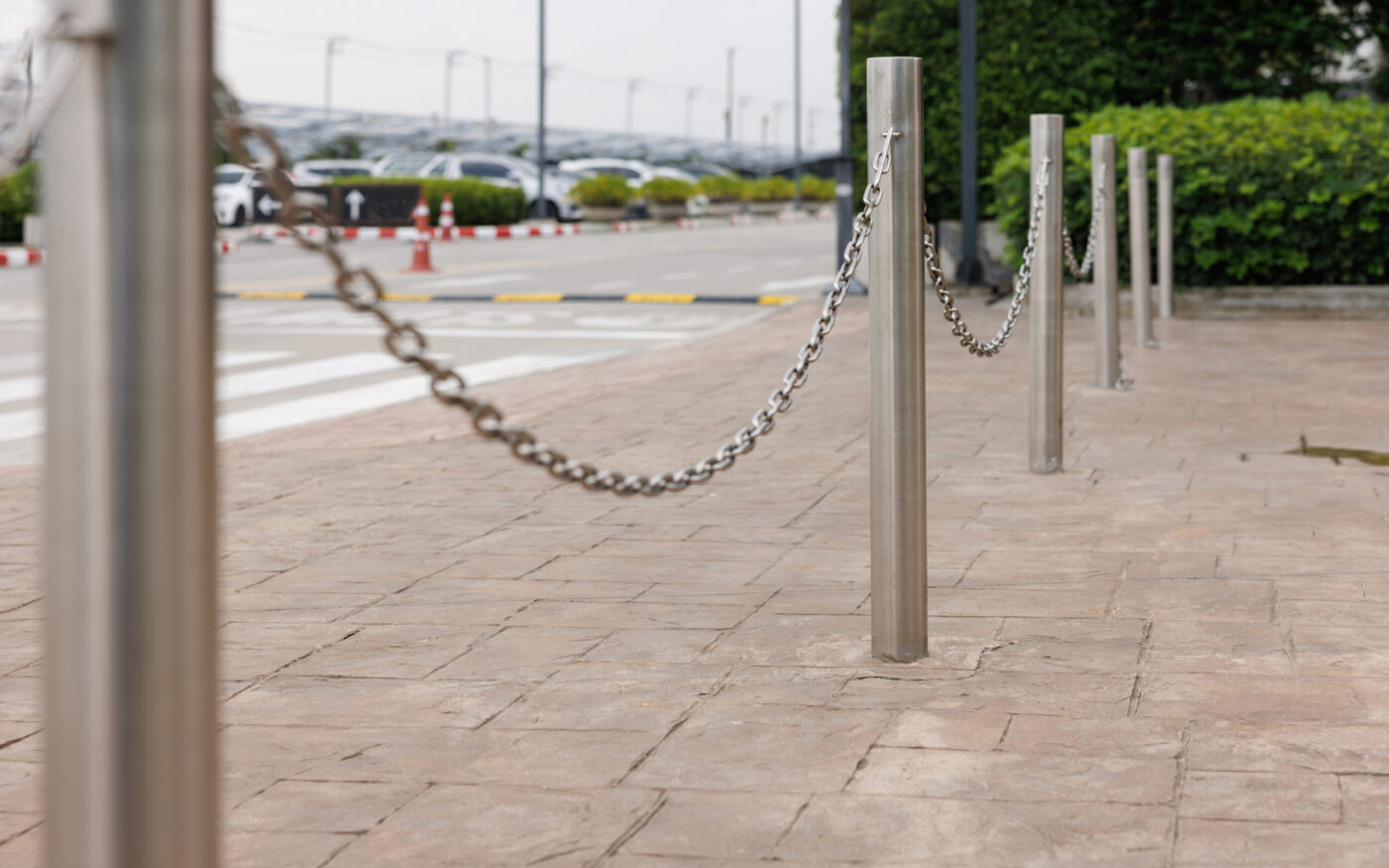 stainless steel bollards with metal chain on concrete pavement.