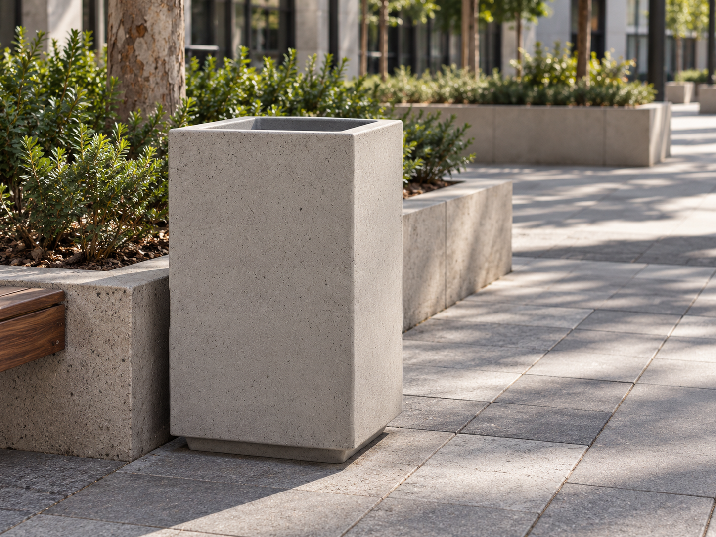 Papelera urbana de hormigón gris con diseño rectangular y acabado de piedra natural, instalada en una plaza moderna con jardineras y zonas ajardinadas
